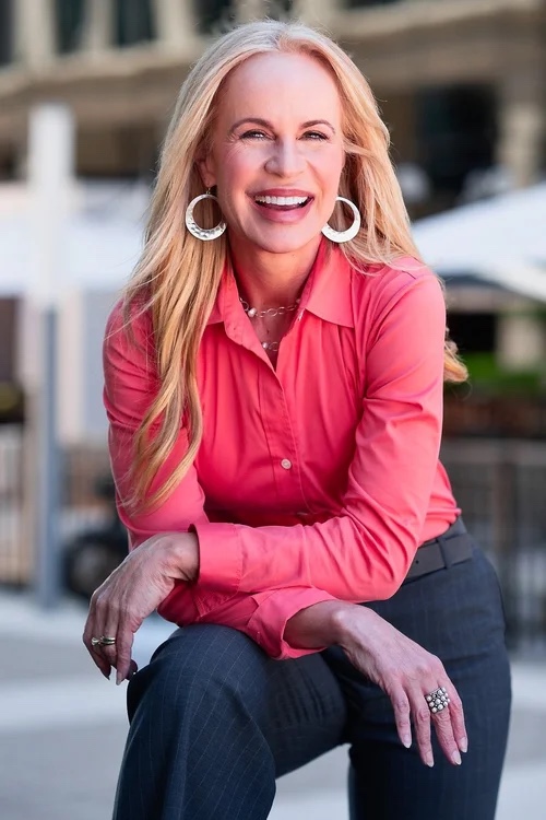 Keynote speaker Elisabeth Leamy seated in a coral blouse, smiling toward the camera.