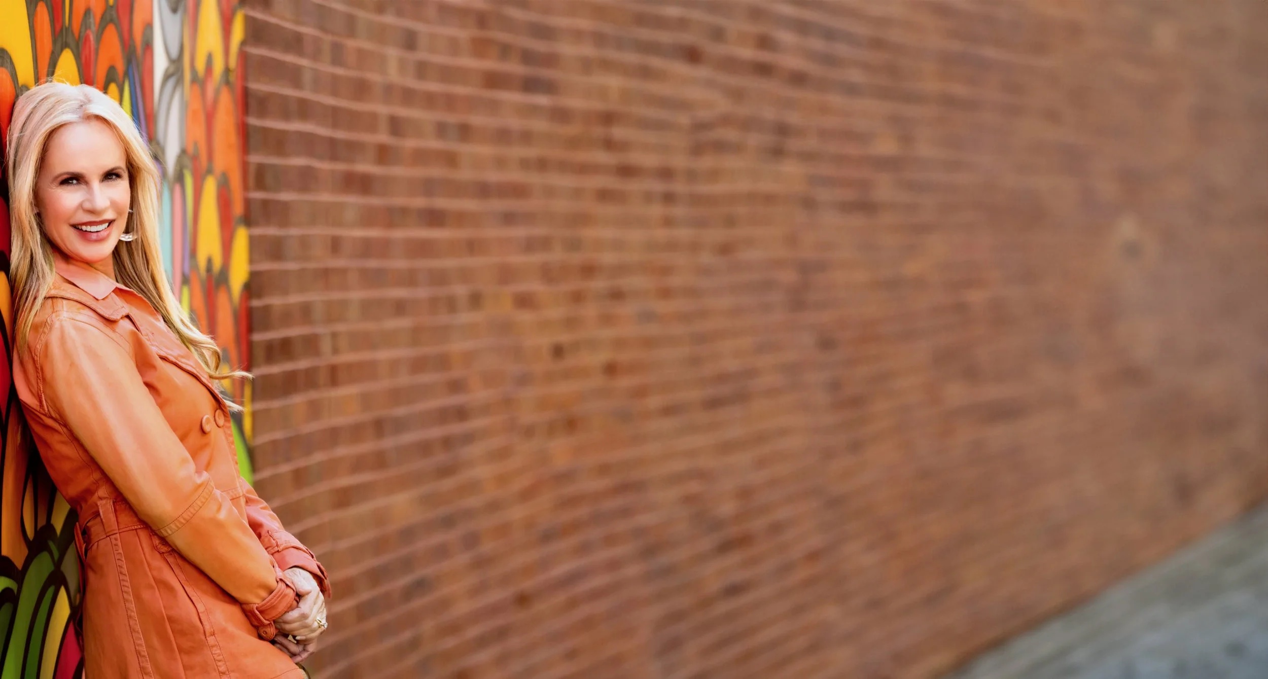 Elisabeth Leamy in orange beside a colorful mural and a long brick wall.