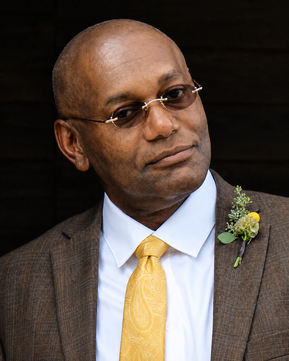 Portrait of Len Cooper wearing a brown suit and yellow tie.